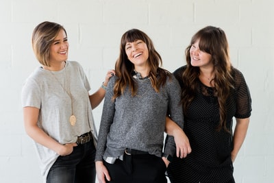 三个女人微笑着站在白墙旁边